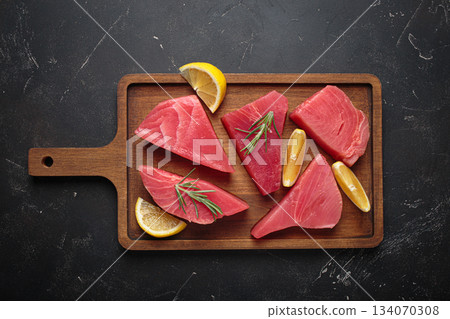 Raw tuna fish steaks fillet rosemary lemon wooden cutting board black background healthy Raw tuna fish steaks fillet rosemary lemon wooden cutting board black background healthy 134070308