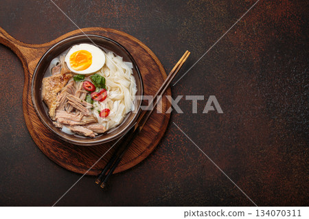 Asian soup rice noodles duck meat egg chopsticks ramen bowl dark rustic background copy space 134070311