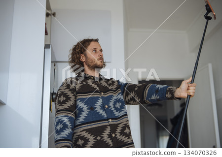 Individual engaged in ceiling painting with long tool in kitchen 134070326