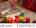 Children's hands paint wooden toy Christmas tree with candles on table 134070422