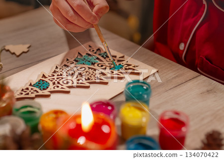 Children's hands paint wooden toy Christmas tree with candles on table 134070422