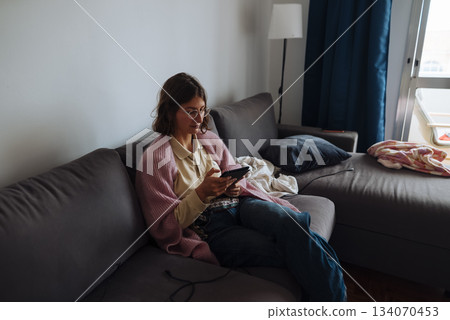Casual woman using phone in comfortable living room setting Casual woman using phone in comfortable living room setting 134070453