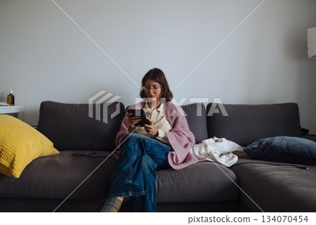 Woman reclined on sofa cuddling small dog while browsing phone Woman reclined on sofa cuddling small dog while browsing phone 134070454