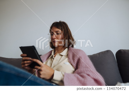 caucasian woman lounging with tablet under blanket, content creator 134070472