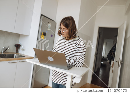 Relaxed woman carefully creates articles in cozy kitchen space 134070473