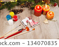 Red color wooden toy skates with paint, brushes, spruce branches, pinecones and candles on table 134070835