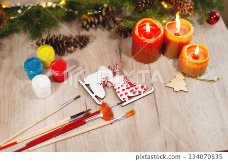 Red color wooden toy skates with paint, brushes, spruce branches, pinecones and candles on table 134070835