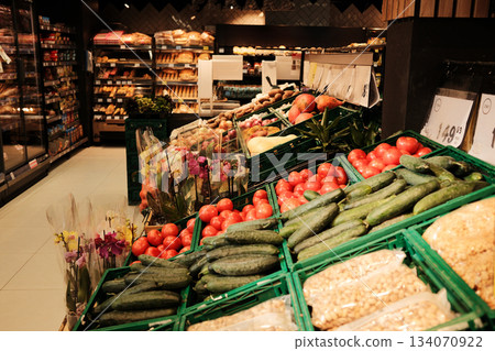 A wide produce section displays tomatoes, cucumbers, roots, and flowers under warm market lighting. The scene reflects abundance, freshness, and daily shopping 134070922