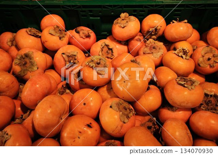 Bright orange persimmons piled in a market crate create a rich seasonal display. The scene highlights freshness, natural color, and organic produce Bright orange persimmons piled in a market crate create a rich seasonal display. The scene highlights freshness, natural color, and organic produce 134070930