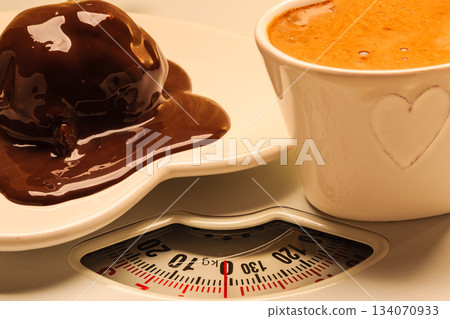 Coffee and chocolate cake on weighing scale. Coffee and chocolate cake on weighing scale. 134070933