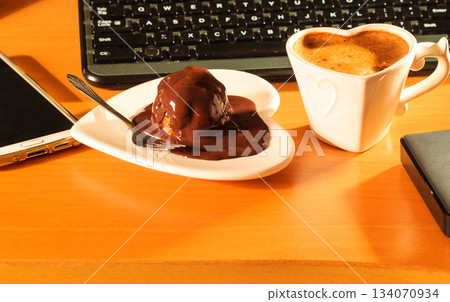 Cup of coffee and chocolate cake next to computer. Cup of coffee and chocolate cake next to computer. 134070934