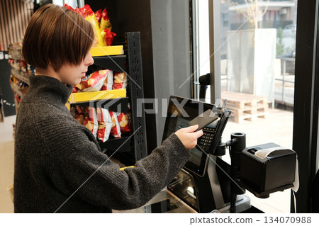 A woman pays with a contactless card at a self-checkout terminal in a supermarket. The concept highlights modern retail technology and convenient consumer experience A woman pays with a contactless card at a self-checkout terminal in a supermarket. The concept highlights modern retail technology and convenient consumer experience 134070988