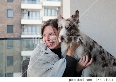 A woman holds her dog closely on a balcony, smiling with warmth and affection. The scene shows trust, companionship, and a tender connection between human and pet A woman holds her dog closely on a balcony, smiling with warmth and affection. The scene shows trust, companionship, and a tender connection between human and pet 134071004