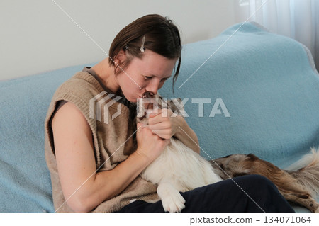 A woman kisses her border collie while holding the dog close on the sofa. The scene expresses warmth, love, and emotional connection between pet and owner A woman kisses her border collie while holding the dog close on the sofa. The scene expresses warmth, love, and emotional connection between pet and owner 134071064