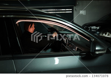 A woman starts reversing inside a garage with a rear-view camera display showing the parking lines. The moment highlights safe maneuvering and modern car technology 134071078