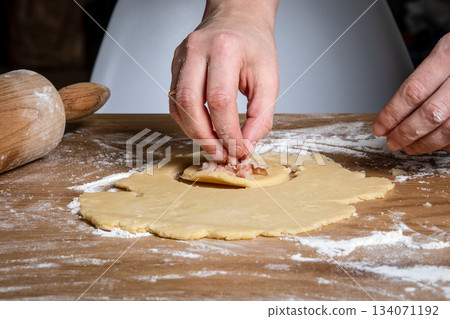 Hands Folding Dough Over Meat Filling on a Floured Wooden Surface 134071192