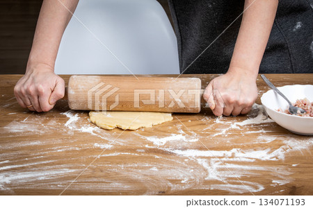Hands Rolling Out Dough on Floured Wooden Surface for Homemade Pastry Preparation 134071193