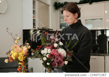 A woman holds a colorful bouquet in a bright kitchen, arranging fresh flowers and adding natural beauty to her home environment 134071367