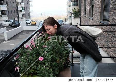 A woman leans over blooming pink flowers, enjoying their scent in a residential courtyard. The image conveys calmness, nature connection, and a peaceful break A woman leans over blooming pink flowers, enjoying their scent in a residential courtyard. The image conveys calmness, nature connection, and a peaceful break 134071376
