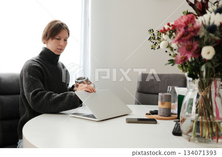 A woman opens her laptop at a white table with flowers nearby, preparing to begin her work in a bright and peaceful room A woman opens her laptop at a white table with flowers nearby, preparing to begin her work in a bright and peaceful room 134071393