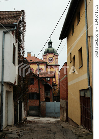 A tall clock tower rises above a narrow residential street with old houses. The view highlights small town charm and history. Sremski Karlovci town in Serbia in autumn season A tall clock tower rises above a narrow residential street with old houses. The view highlights small town charm and history. Sremski Karlovci town in Serbia in autumn season 134071515