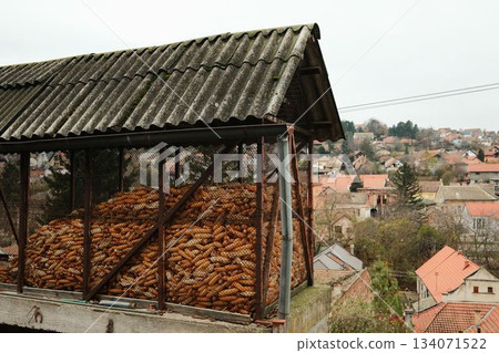 A raised mesh storage filled with dried corn cobs. The scene shows rural life and traditional farming over rooftops 134071522