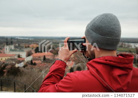 Traveler holds a smartphone and records the view of church towers and rooftops from a high point. The moment shows discovery and connection. Travel blogger concept Traveler holds a smartphone and records the view of church towers and rooftops from a high point. The moment shows discovery and connection. Travel blogger concept 134071527