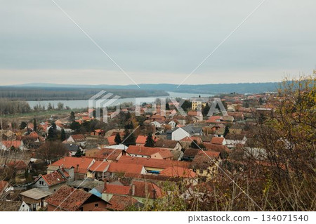 Wide view of Sremski Karlovci with red rooftops and riverbank landscape under grey autumn sky. The moment shows peace and slow travel Wide view of Sremski Karlovci with red rooftops and riverbank landscape under grey autumn sky. The moment shows peace and slow travel 134071540