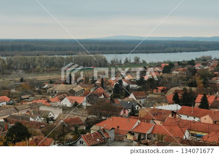 A wide view of Sremski Karlovci stretches toward the river and distant forest line. In the distance, a modern train can be seen racing along the Danube railway 134071677
