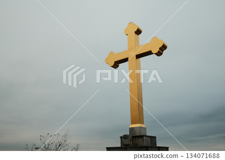 Close view of a golden Orthodox cross rising against a cloudy sky in Sremski Karlovci. A symbolic scene highlighting religion and heritage Close view of a golden Orthodox cross rising against a cloudy sky in Sremski Karlovci. A symbolic scene highlighting religion and heritage 134071688
