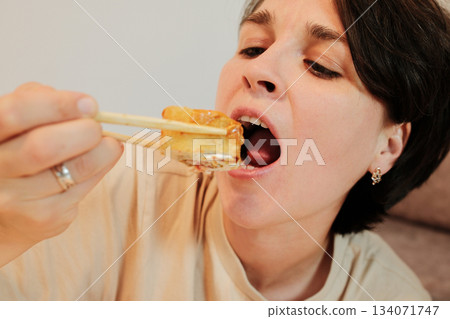 A close-up view of a woman opening her mouth to eat a fried sushi roll held with chopsticks. The shot focuses on appetite, taste, and an expressive dining moment 134071747