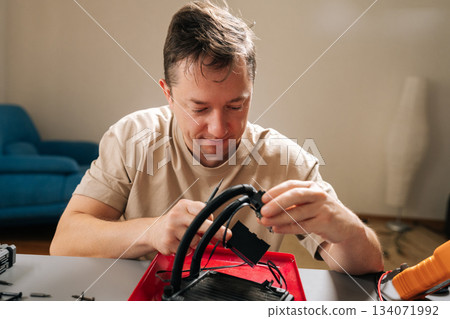Portrait of professional repairman repairing and inspecting all-in-one pc liquid cooler at home, servicing radiator, pump and tubing to maintain performance and upgrade desktop cooling system. Portrait of professional repairman repairing and inspecting all-in-one pc liquid cooler at home, servicing radiator, pump and tubing to maintain performance and upgrade desktop cooling system. 134071992