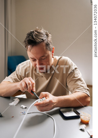Vertical portrait of man repairing broken electrical cable with screwdriver, handling wires and components, embodying concepts of problem-solving, handyman work, and home improvement. Vertical portrait of man repairing broken electrical cable with screwdriver, handling wires and components, embodying concepts of problem-solving, handyman work, and home improvement. 134072036