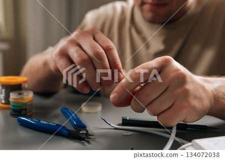 Close-up of male hands working on electrical wires, stripping insulation and connecting power cable to controller, symbolizing repair, installation and technical support for electronic components. Close-up of male hands working on electrical wires, stripping insulation and connecting power cable to controller, symbolizing repair, installation and technical support for electronic components. 134072038