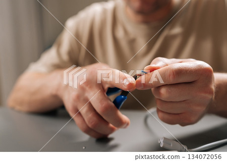 Close-up of male hands fixing damaged electrical cable at workbench, stripping outer insulation with wire stripper tool, performing diy repair on electronics and home appliances. Close-up of male hands fixing damaged electrical cable at workbench, stripping outer insulation with wire stripper tool, performing diy repair on electronics and home appliances. 134072056