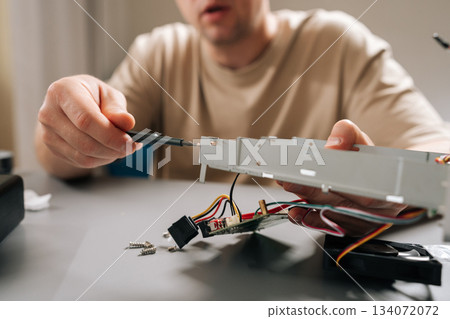 Closeup shot of technician male performing computer repair, using screwdriver to fix open electronics hardware, servicing device components at workbench. Concept of technical support and maintenance. Closeup shot of technician male performing computer repair, using screwdriver to fix open electronics hardware, servicing device components at workbench. Concept of technical support and maintenance. 134072072
