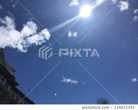 Contrails and the sun crossing the blue sky 134072395