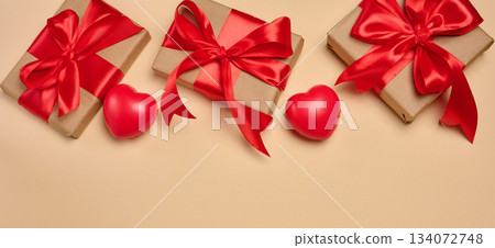 Gifts wrapped in red satin ribbon with a bow on a beige background Gifts wrapped in red satin ribbon with a bow on a beige background 134072748