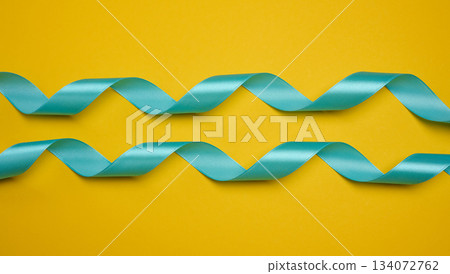 Blue satin ribbon, curved into a wave, centered on a yellow background. Concept for gift, decoration, and celebration. 134072762