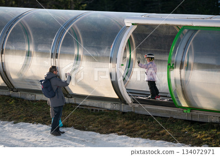 A girl on skis stands on a carpet ski lift in a glass tunel A girl on skis stands on a carpet ski lift in a glass tunel 134072971