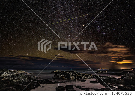 A meteor-filled night sky shining over a starry coastline A meteor-filled night sky shining over a starry coastline 134073536