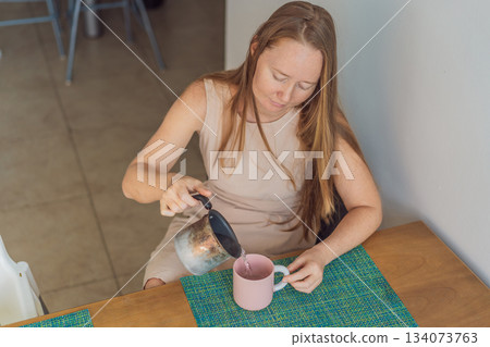 Woman enjoying a peaceful breakfast at the table in a bright home interior, starting her morning with calm energy. Healthy lifestyle, morning routine and wellbeing concept, representing self-care 134073763