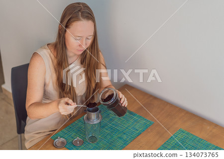 Woman enjoying a peaceful breakfast at the table in a bright home interior, starting her morning with calm energy. Healthy lifestyle, morning routine and wellbeing concept, representing self-care 134073765