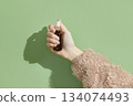 A womans hand holding a brown bottle of serum on a green background 134074493