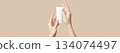 A womans hands holding a white cosmetic tube on a beige background. Beauty treatment concept 134074497