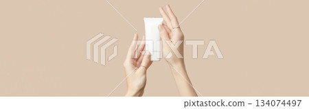 A womans hands holding a white cosmetic tube on a beige background. Beauty treatment concept A womans hands holding a white cosmetic tube on a beige background. Beauty treatment concept 134074497