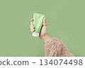 A womans hand in a sweater holds a tube of cream on a green background. Self care beauty treatment 134074498