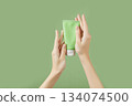 A womans hands holding a tube of lotion on a green background. Body care 134074500