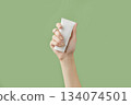 A womans hand holding a white cosmetic tube on a green background 134074501