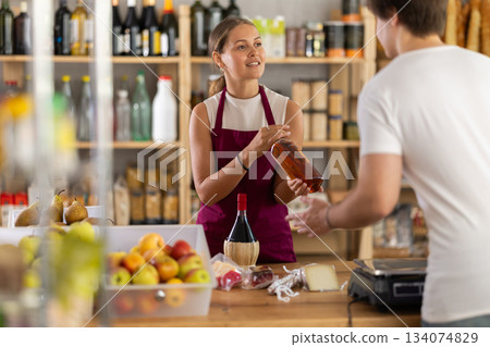 Friendly female salesperson offers to buy bottle of whiskey to male customer at grocery store 134074829